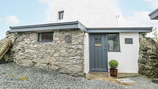 A stone building with a grey door and a small window, labeled "Keen Glell The Old Cornwall."