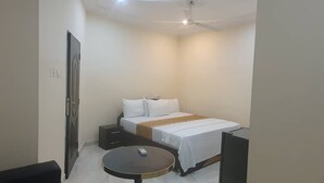 A small, clean room with a bed, bedside table, and a round table. - Bluefin Hotel (Somanya)