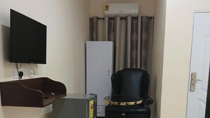 A compact room with a flat-screen TV mounted on the wall, a small refrigerator, a chair, and a bed. - Bluefin Hotel (Somanya)