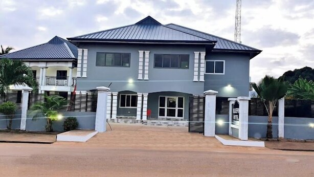 A two-story building with a grey facade, a metal roof, and a gated entrance. - Bluefin Hotel (Somanya)