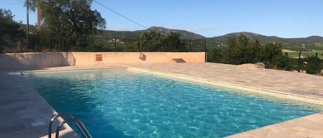 A rectangular outdoor swimming pool with clear blue water, surrounded by a tiled deck.