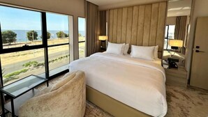 Une chambre d’hôtel avec un grand lit, un bureau et une vue sur la plage et la route.