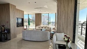 Un salon moderne avec un canapé aux lignes courbes, une table basse et un téléviseur. Une grande fenêtre offre une vue sur la ville.