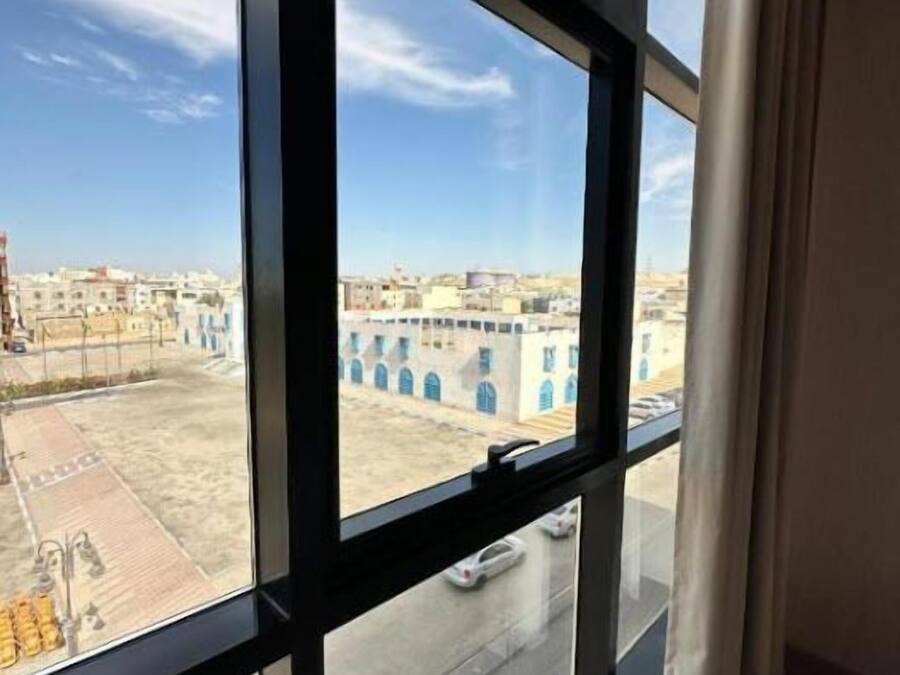 A room with a large window offering a view of a cityscape with buildings and a clear sky.