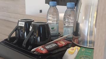 A hotel room with a minibar containing a coffee maker, water bottles, a Nescafe coffee packet, and a box of ice cream.