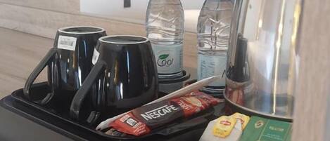 A hotel room with a minibar containing a coffee maker, water bottles, a Nescafe coffee packet, and a box of ice cream.