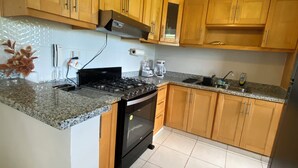 A kitchen with wooden cabinets, a granite countertop, a stove, and a sink. - Cozy apartment with style and swimming pool (Villa Hermosa)