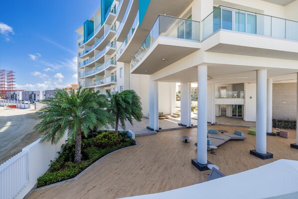 A modern hotel with a curved facade, outdoor seating areas, and palm trees.