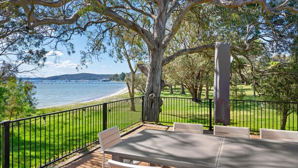 A patio with a table and chairs overlooking a body of water and a distant shoreline.