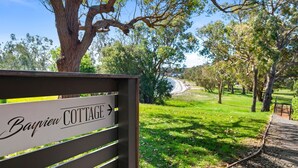 A sign for Bayville Cottage with a view of a grassy area and trees.