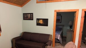 Una sala de estar acogedora con un sofá marrón, una mesa de centro de madera y una silla. Hay dos cuadros enmarcados en la pared.