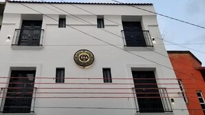 Een gebouw met een witte gevel, een centraal geplaatst rond embleem en meerdere ramen.