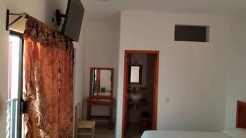 Une chambre à coucher comprenant un lit, un téléviseur fixé au mur, une chaise et une petite salle de bain avec un lavabo et un miroir.