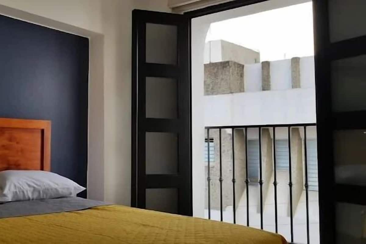 Une chambre à coucher avec un lit, une tête de lit en bois et une vue sur l’extérieur grâce à une grande fenêtre.