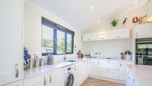Une cuisine moderne avec des meubles blancs, un lave-linge encastré, une fenêtre offrant une belle vue et un parquet en bois disposé en chevrons.
