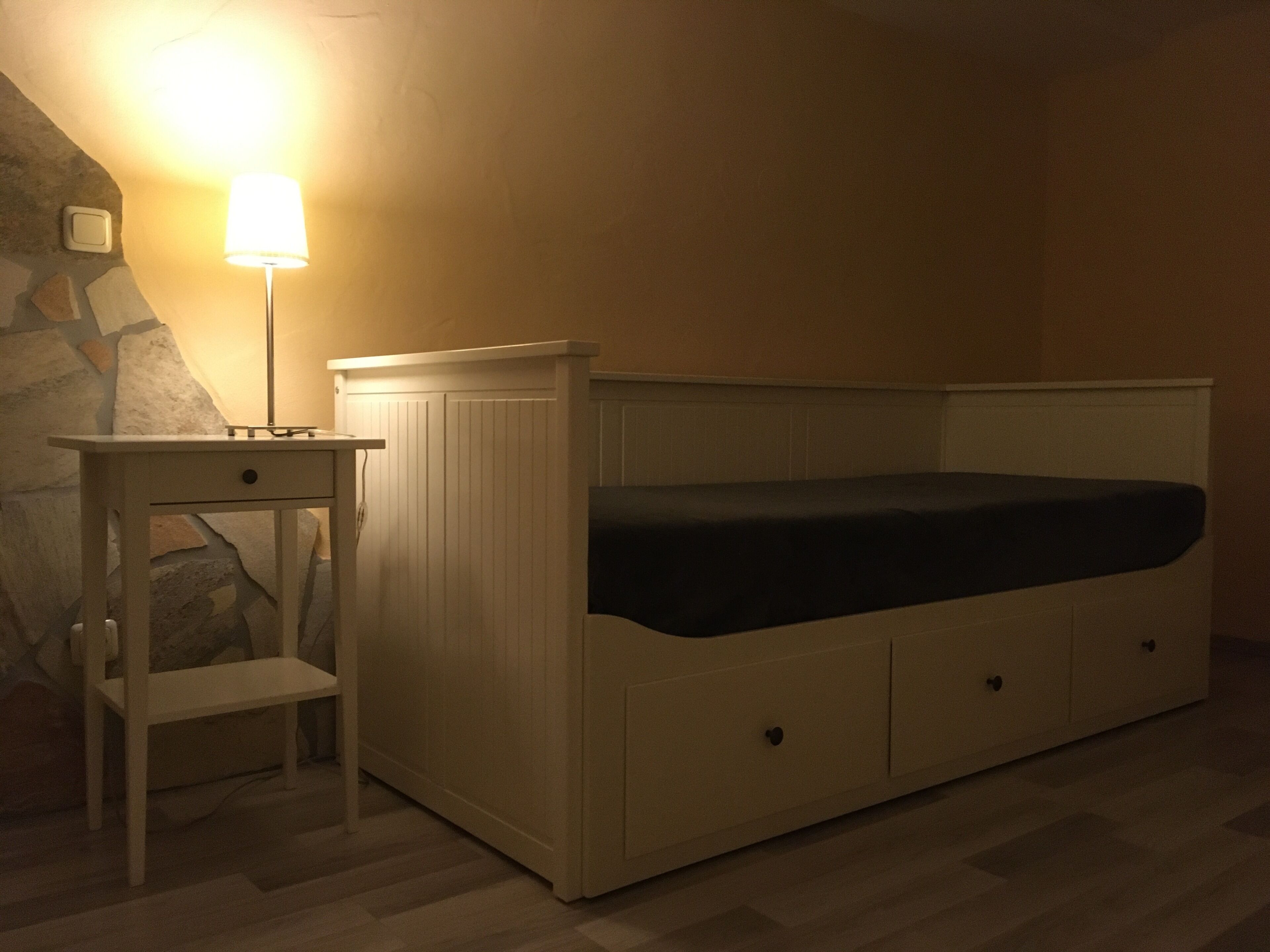 Une petite chambre avec un lit simple, une table de chevet et une lampe.