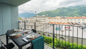 A balcony with a table set for dining, overlooking a parking area and buildings with a mountainous backdrop.