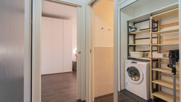 A laundry room with a washing machine, wooden shelves, and a door leading to another room.