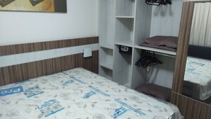 Une chambre à coucher comprenant un lit, une armoire, un miroir et une étagère avec des cintres.