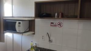 Une cuisine équipée d’un four à micro-ondes, d’un évier et d’une étagère sur laquelle se trouvent une bouilloire et un récipient.