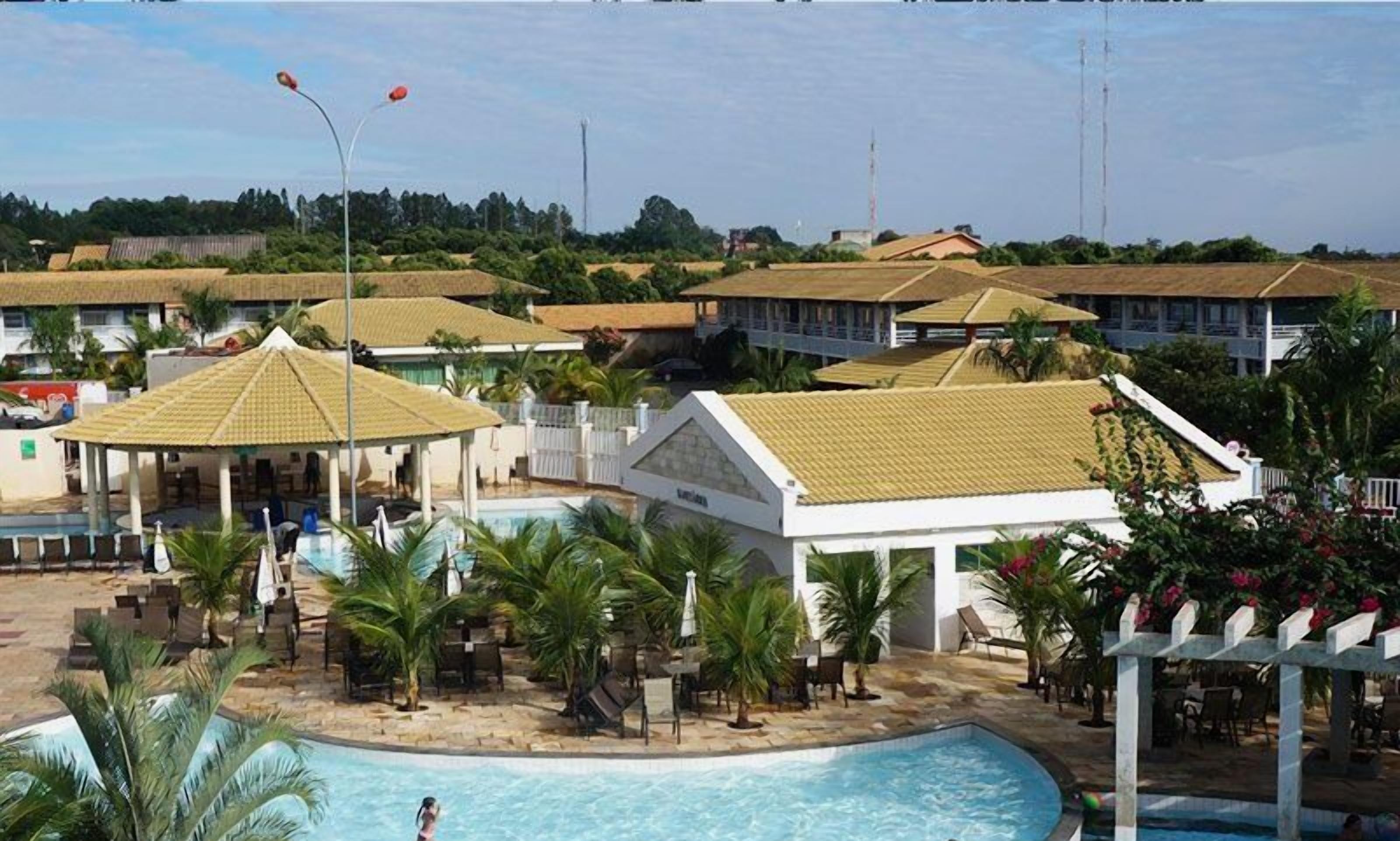 Un resort con piscina, zonas de descanso y varias construcciones con techos de paja.
