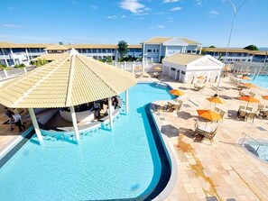 Una piscina de borde curvo, con tumbonas, sombrillas y un edificio de fachada blanca al fondo.