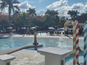 Un espace piscine agrémenté de chaises longues et de parasols, entouré de palmiers et surplombé d’un ciel dégagé.