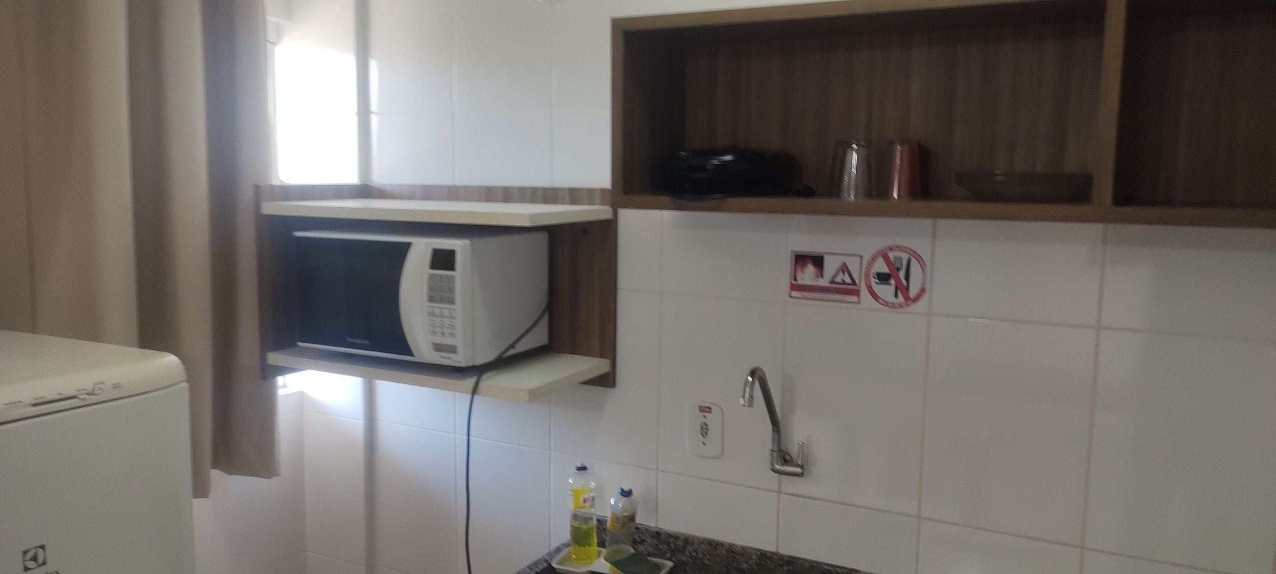 Una cocina con microondas, un lavamanos y una repisa con tetera y un recipiente.