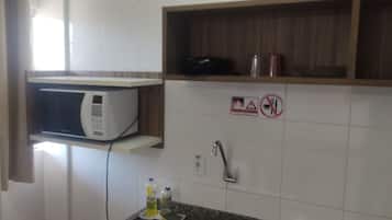 Una cocina con microondas, un lavamanos y una repisa con tetera y un recipiente.