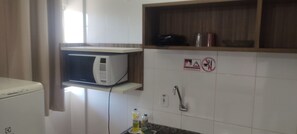 A kitchen with a microwave, a sink, and a shelf with a kettle and a container. - Lacqua Di Roma via Roberto Imoveis (Caldas Novas)