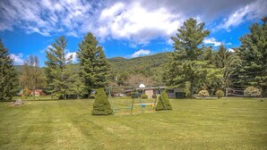 A grassy outdoor area with a swing set, a small building, and trees in the background.