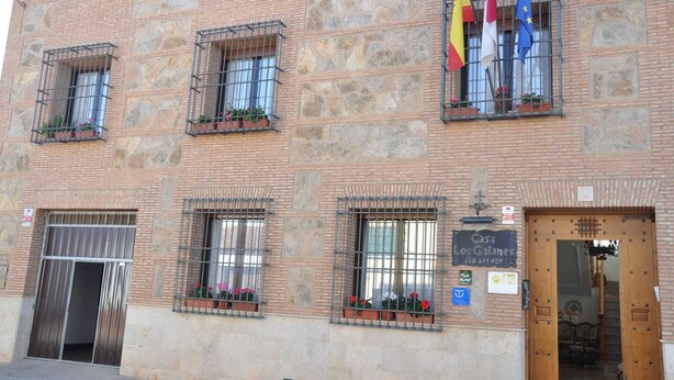 A building with stone facade, multiple windows with metal grilles, and flags. - Los galanes  (Villanueva de los Infantes)