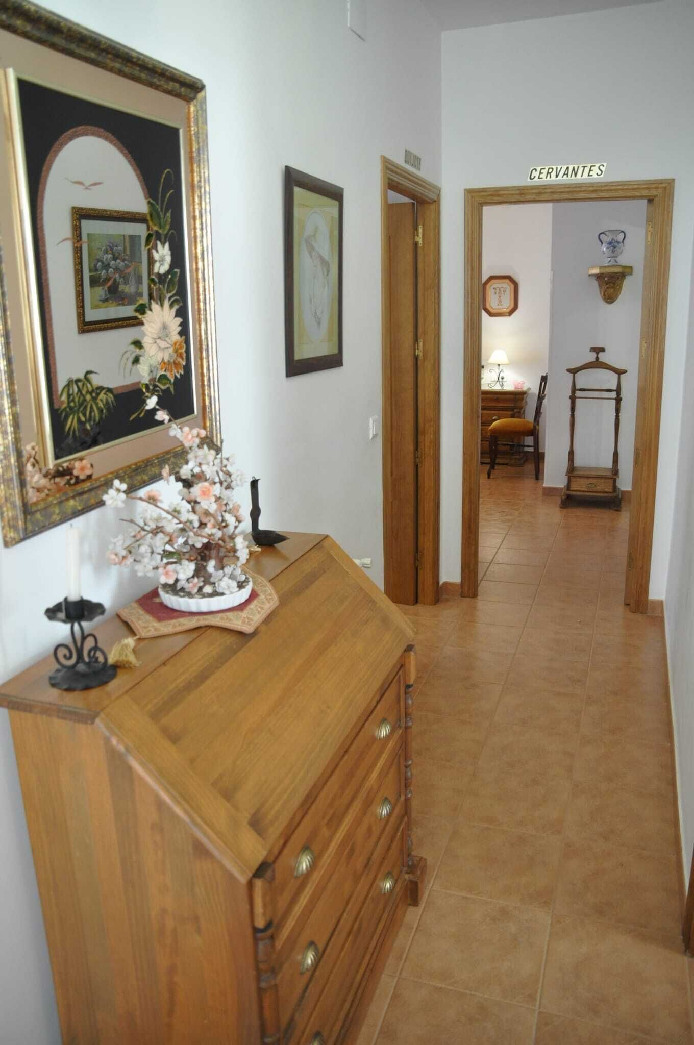 Un passadís amb un armari de fusta, un mirall i una porta amb la inscripció "CERVANTES".