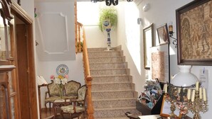 A staircase with a chandelier, a wooden chair, a table with a vase, and a framed picture on the wall. - Los galanes  (Villanueva de los Infantes)