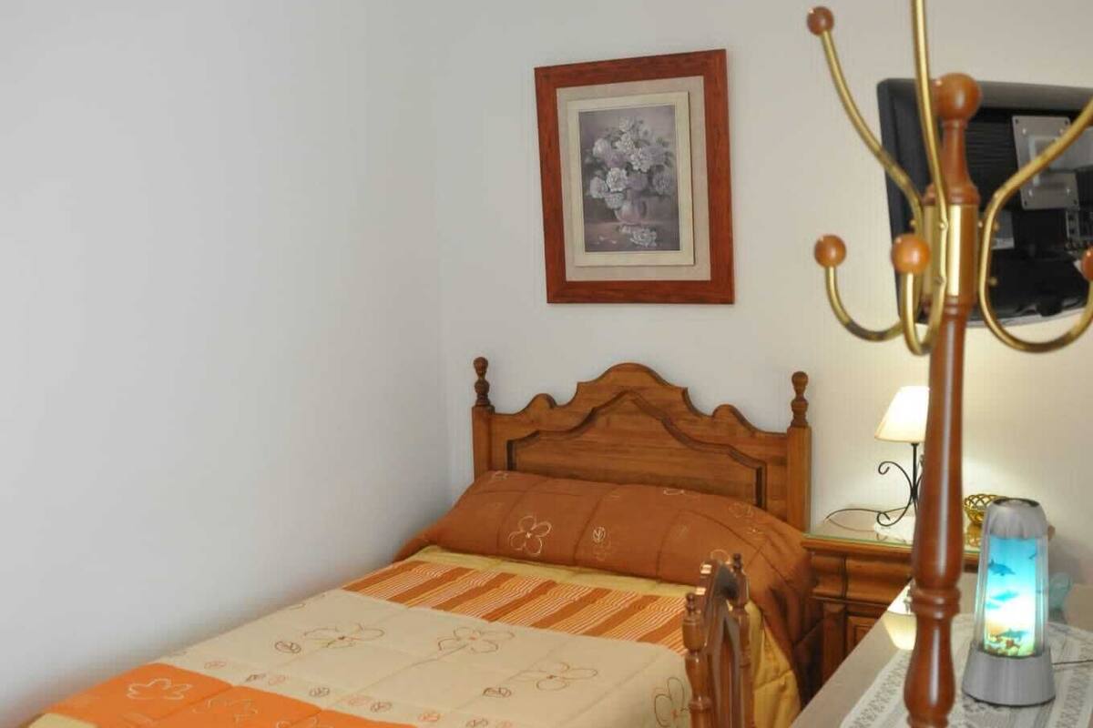 Ein Schlafzimmer mit einem hölzernen Bett, einem Nachttisch mit Lampe, einem Sessel und einem gerahmten Bild an der Wand.