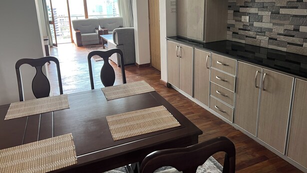 A modern kitchen with wooden cabinets and a black countertop, a dining area with a table and chairs, and a view of the city through large windows. - Delightful 3-bedroom apartment with best view in Addis Ababa (Addis Ababa)