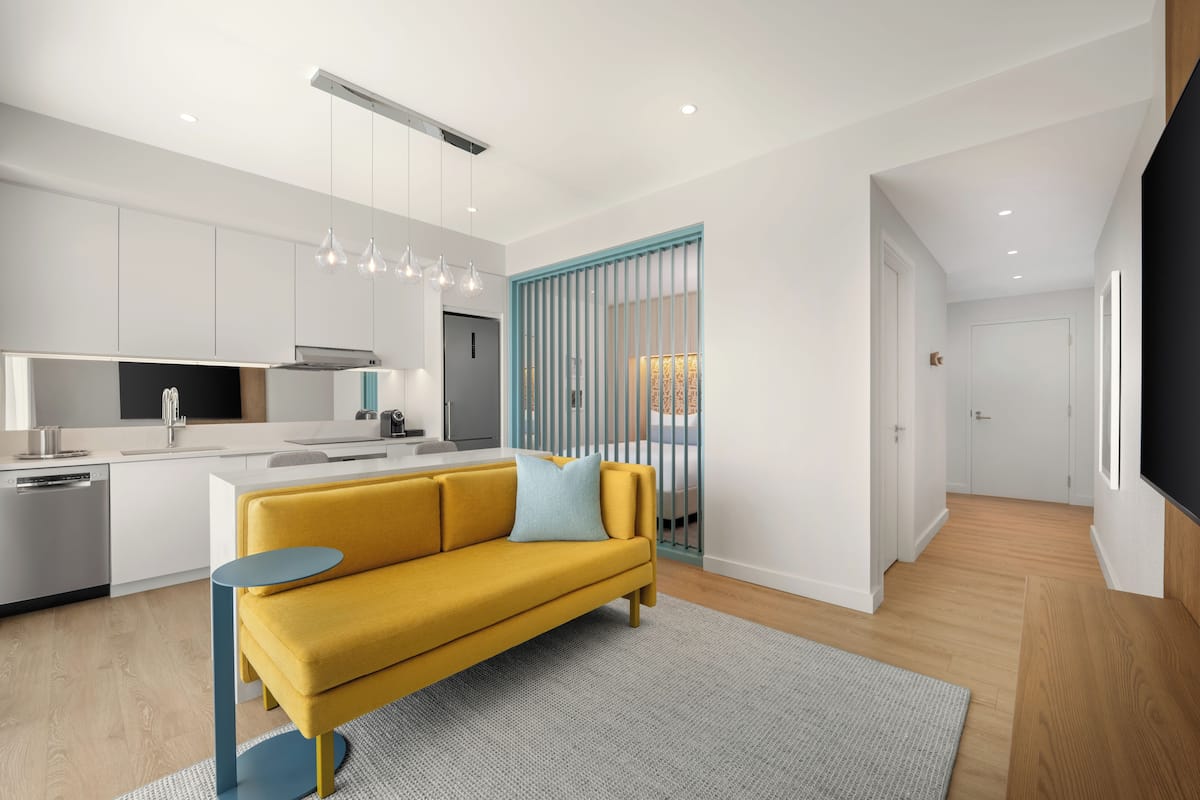 A modern kitchen with white cabinets, a yellow sofa, and a blue accent wall.