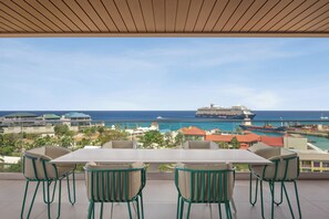 A terrace with a table and chairs, overlooking a coastal area with buildings and a cruise ship. - ONE GT Grand Cayman (George Town)