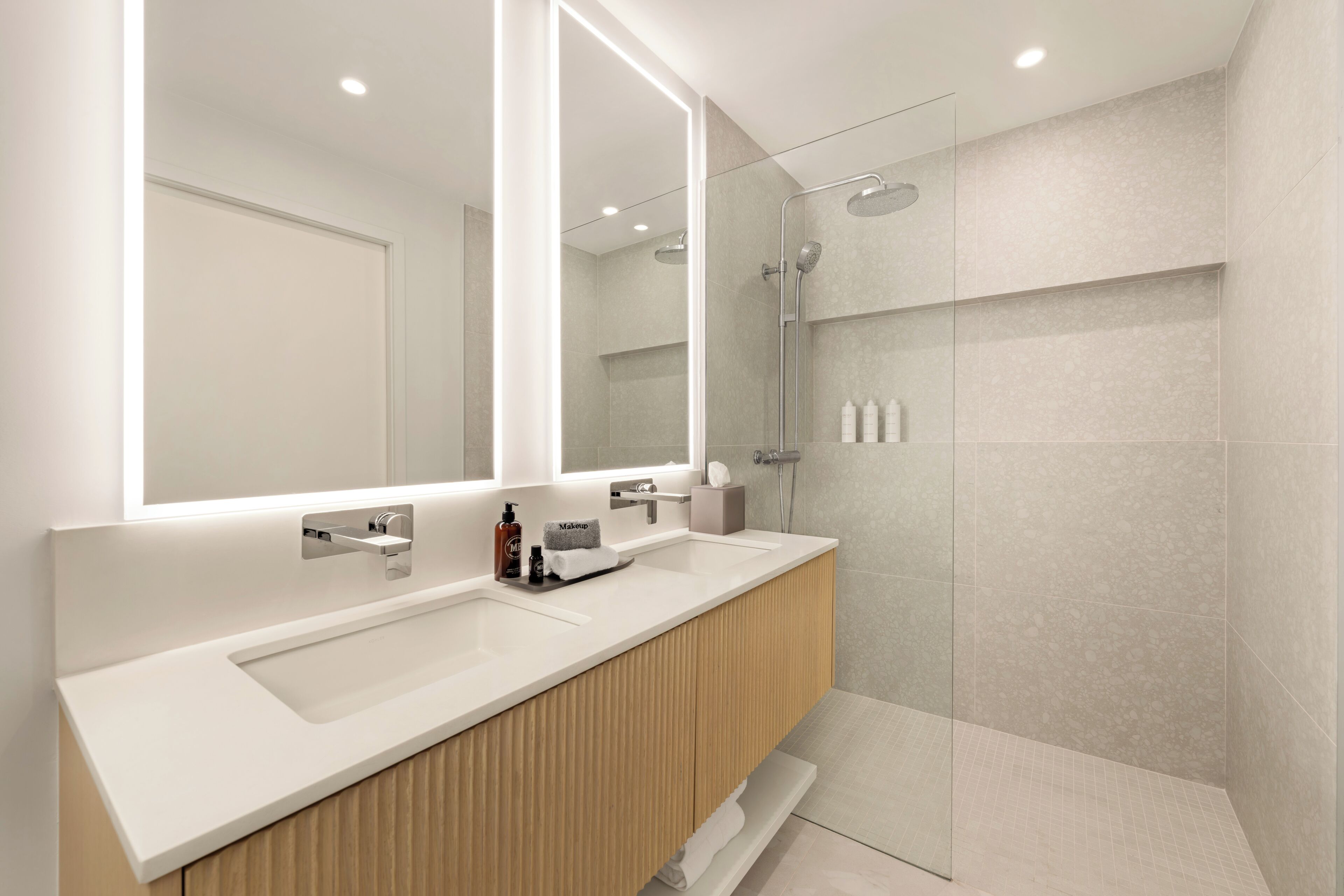 A modern bathroom with a large mirror, two sinks, a shower, and a wooden vanity.