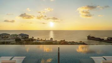 An infinity pool with a view of the ocean and a sunset.