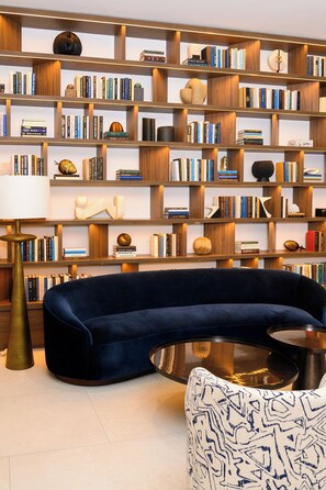 A modern living room with a dark blue sofa, a round coffee table, and a bookshelf filled with books and decorative items. - ONE GT Grand Cayman (George Town)