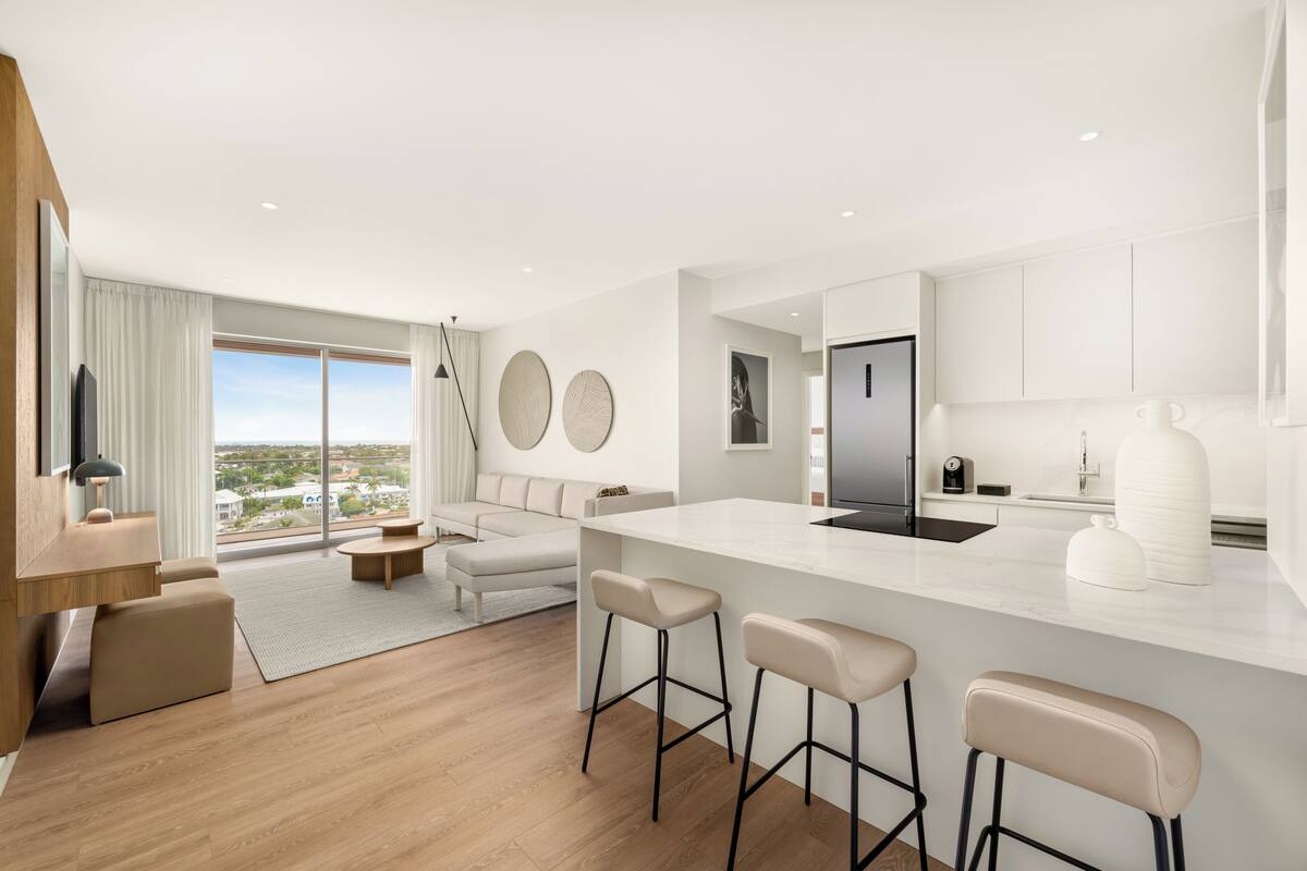 A modern kitchen with a central island, bar stools, and a large window.