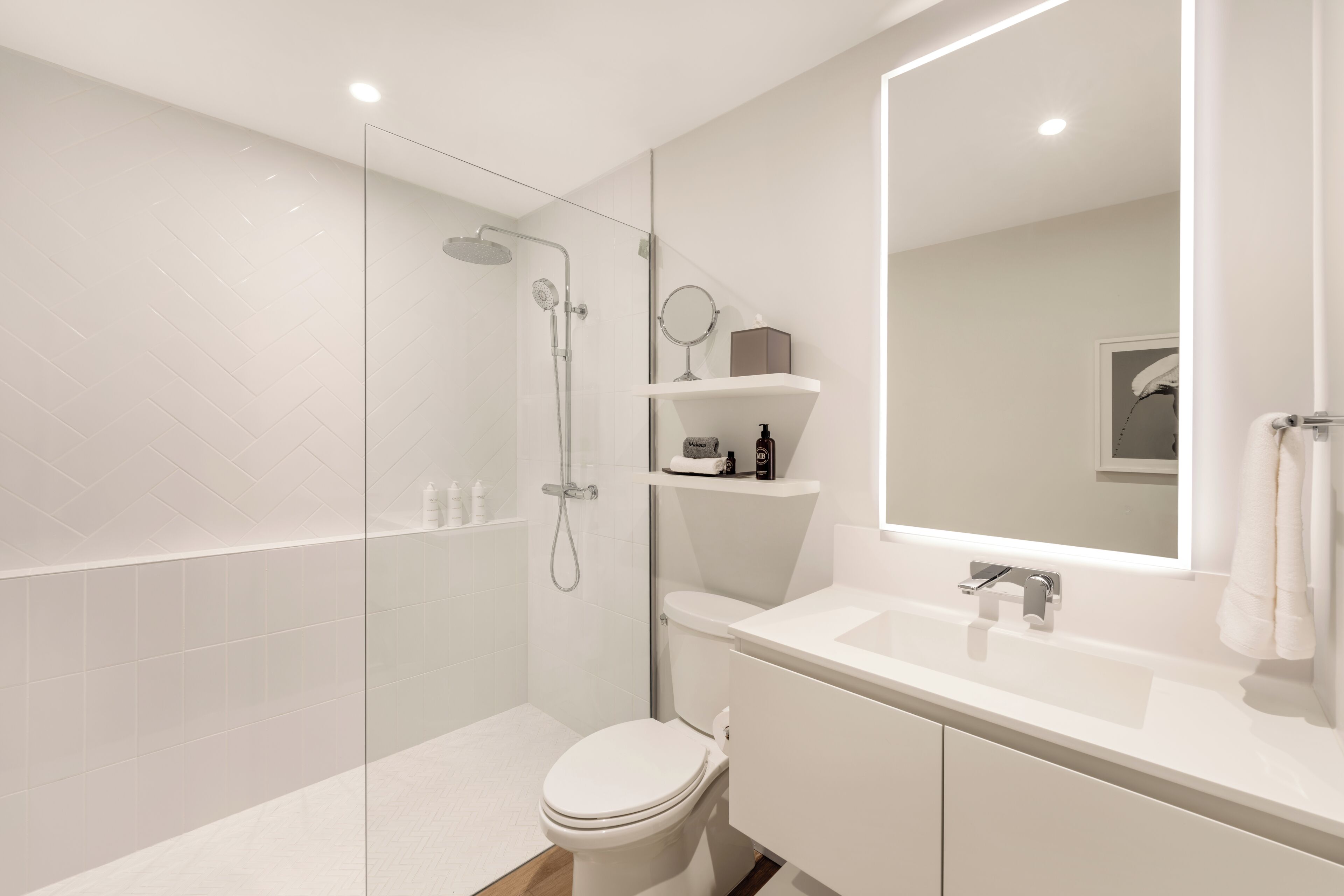 Une salle de bain moderne avec une douche à parois de verre, des toilettes blanches, un lavabo avec un miroir et une étagère contenant des articles de toilette.