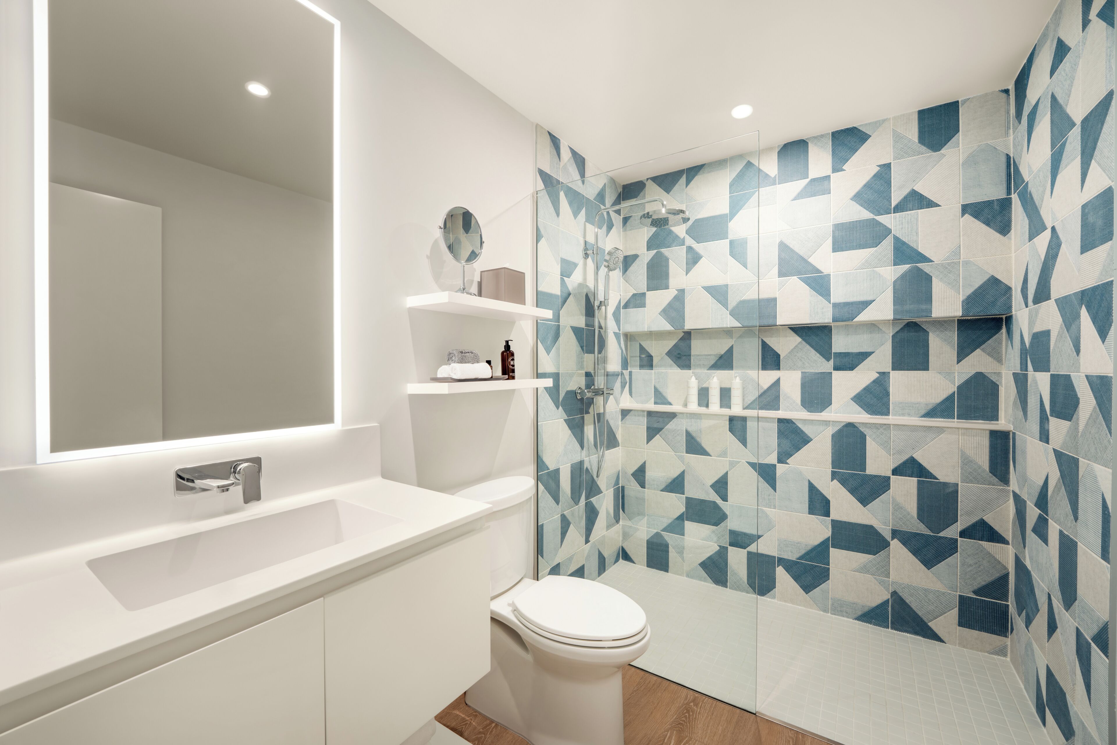 Un baño moderno con un lavamanos blanco, inodoro y ducha con diseños geométricos de azulejos.