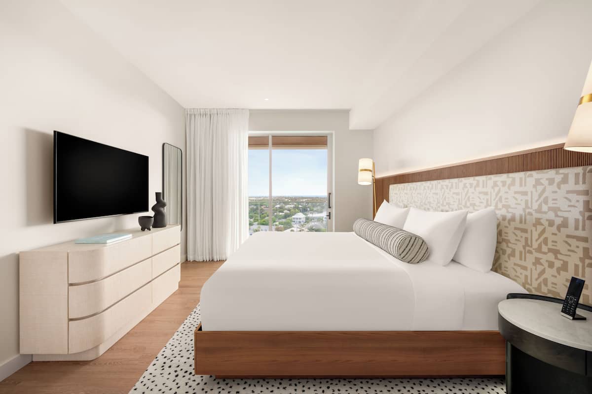 A hotel room with a large bed, a flat-screen TV, a dresser, and a window with a city view.