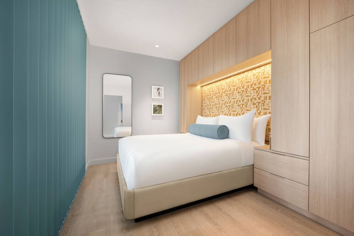 A modern bedroom with a large bed, a wooden headboard, a mirror, and a wall-mounted light fixture.