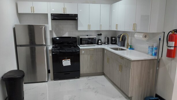 A modern kitchen with white cabinets, stainless steel appliances, and a marble floor. - Spacious 4-bedroom, 4 beds 2 bath each, in lovely Newark with AC, WiFi. (Newark)