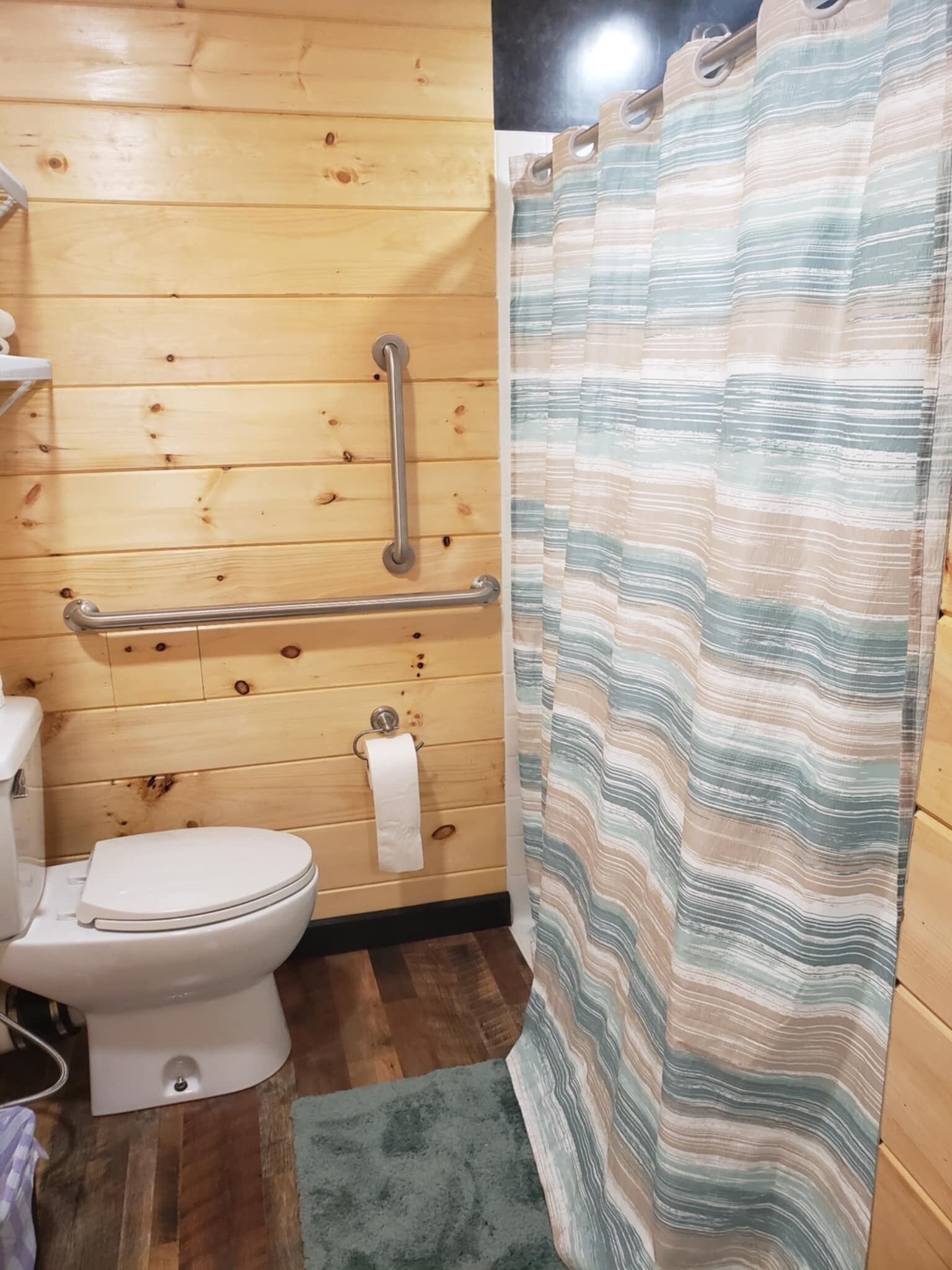 Un baño con paneles de madera, cortina de ducha a rayas, un inodoro y una barra de apoyo.