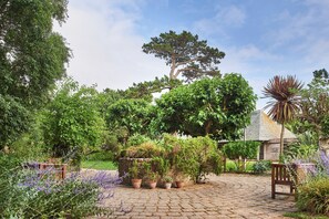 A garden with a paved pathway, potted plants, and a wooden bench. - Les Maisons De Tatihou, The Originals Relais (Saint-Vaast-la-Hougue)