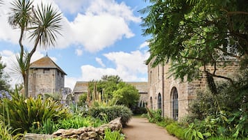 Un bâtiment en pierre, accessible par un chemin, entouré d’une végétation luxuriante et sous un ciel dégagé.